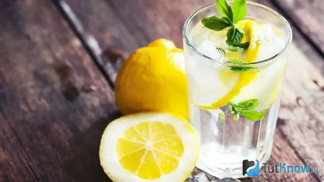 Bir stakan suvda limon bo'laklari va ikkita limon yonma -yon