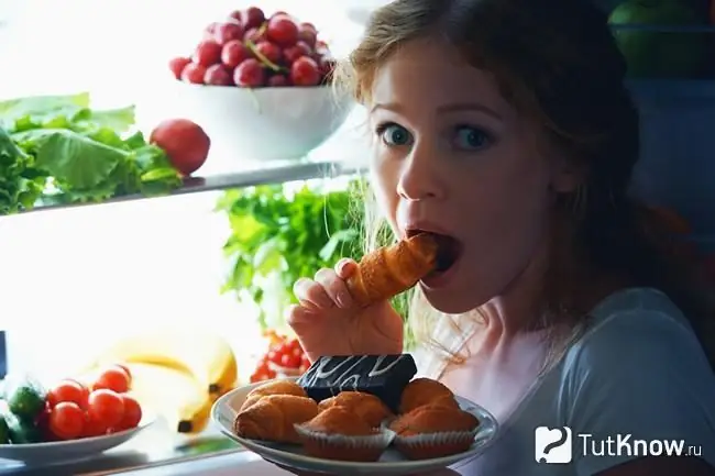 Ragazza che mangia dolci di notte vicino al frigorifero