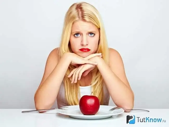 Triste niña sentada frente a un plato con una manzana