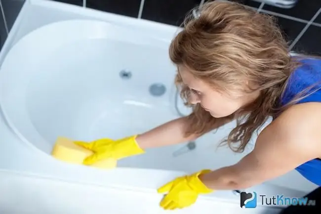 La fille nettoie le bain avec une éponge