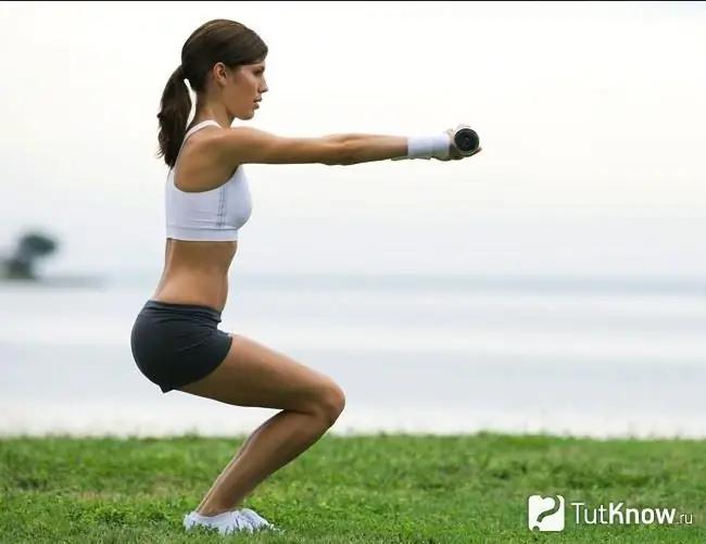 Gadis berjongkok dengan dumbbell di luar rumah