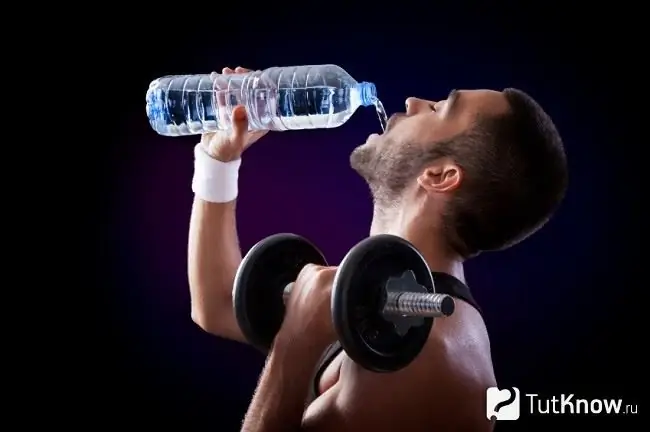 Atlet minum air dengan dumbbell di tangan