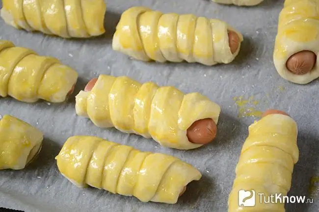 Sausages in dough, greased with yolk, on a baking sheet